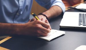 A person is writing notes while working on a computer.